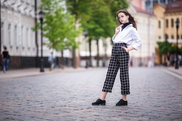 Portrait of little beautiful stylish kid girl with sunglasses and short plaid pants in city urban street