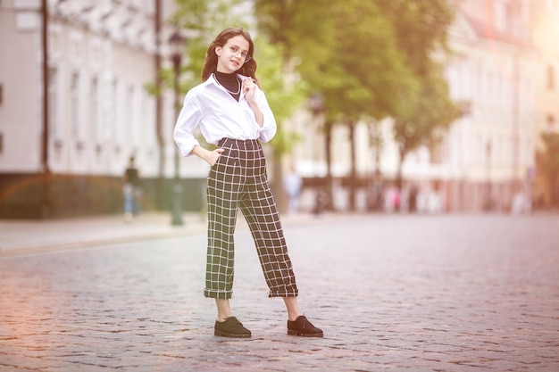 Portrait of little beautiful stylish kid girl with sunglasses and short plaid pants in city urban street