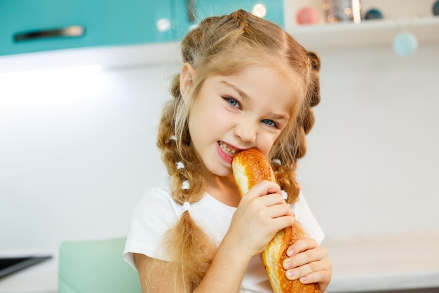 Ritratto di una bambina bionda che morde una baguette fresca