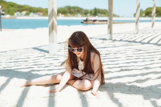 해변의 모래에 앉아 드레스에 어린 금발 소녀의 초상화 여름 화창한 날