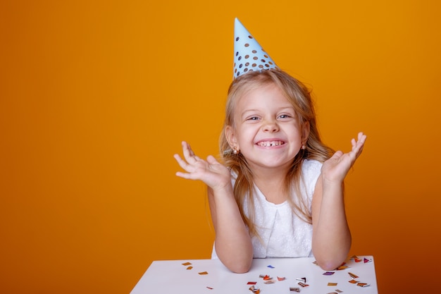 Il ritratto di una bambina bionda in un cappello festivo si rallegra il fondo colorato coriandoli