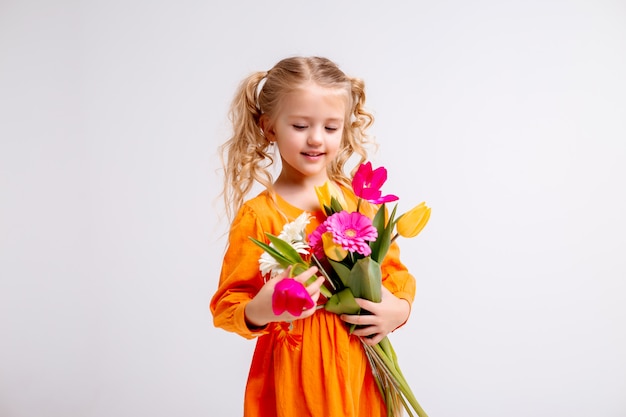 portrait of a little blonde girl with a bouquet of spring flowers on a light wall