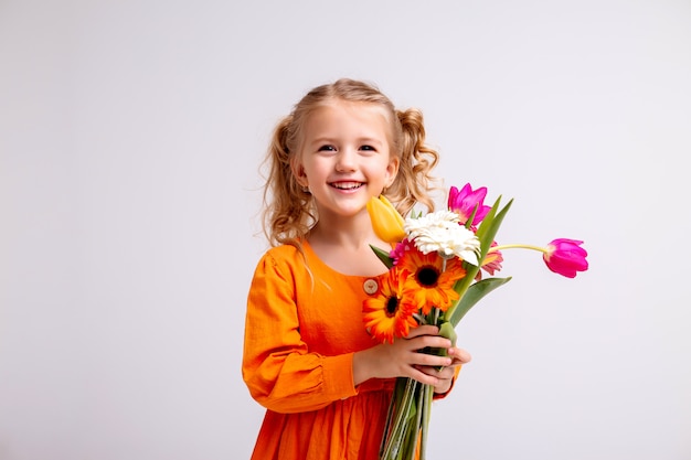 portrait of a little blonde girl with a bouquet of spring flowers on a light wall