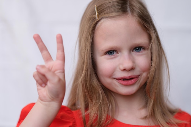 Foto ritratto di bambina bionda con due dita gesto di buon umore e concetto di emozioni infantili