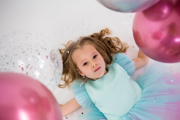 Portrait of a little blonde lying with balloons on a white background. Holiday background