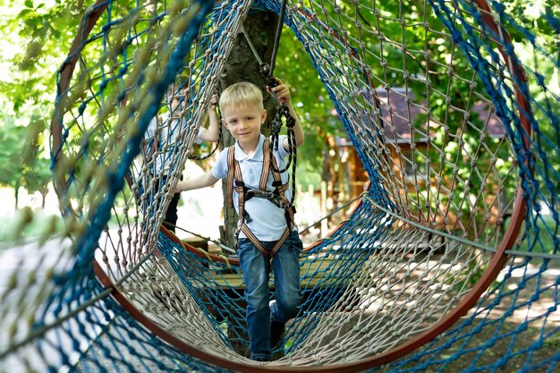 Portrait of a little boy in climbing gear in a rope park, holding a rope with a carbine.