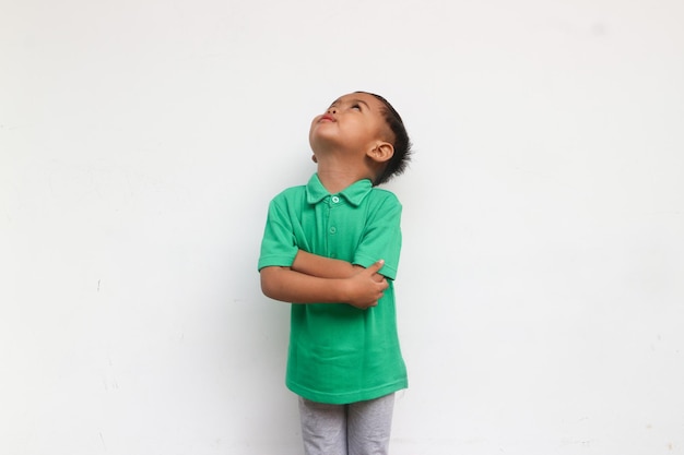 Photo portrait of a little boy curious looking up while crossed his arm isolated on the white background