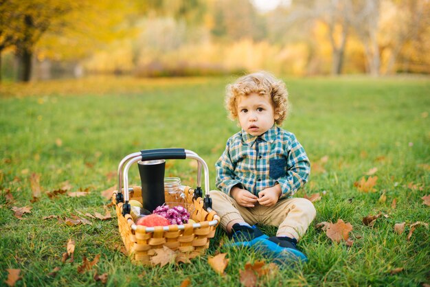 Portrait of little boy outdoor sitting on grass in park, picninc concept