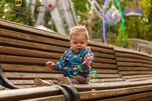 Portrait of a little boy in the park on a bench catching soap bubbles