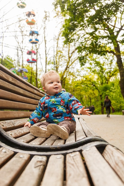 Портрет маленького мальчика в парке на скамейке, ловящего мыльные пузыри