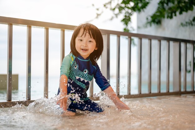 Portrait of little boy in a swiming suit is splashing with his hands in the swimming poolHavin