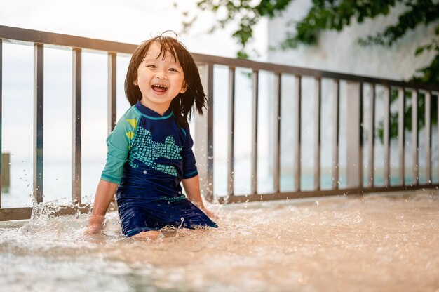 スイミングスーツを着た小さな男の子の肖像画がスイミングプールで彼の手で水しぶきを上げていますハビン