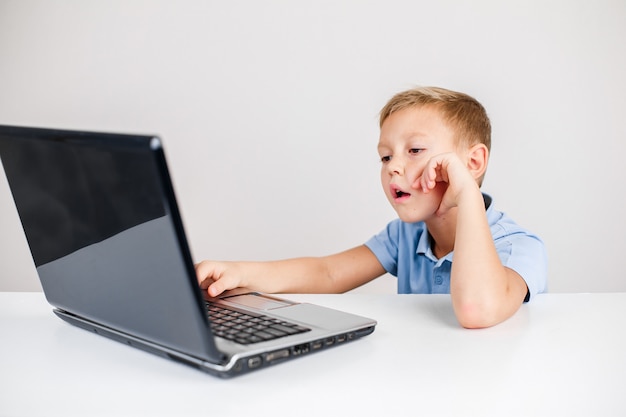 Portrait of little boy with blond hair using laptop at desk