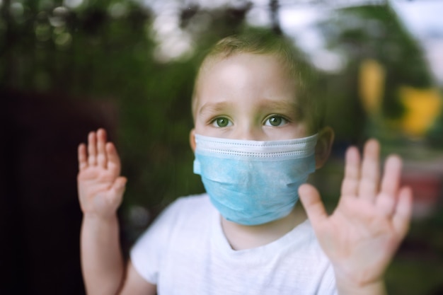 Ritratto di ragazzino con maschera medica che guarda la telecamera in città