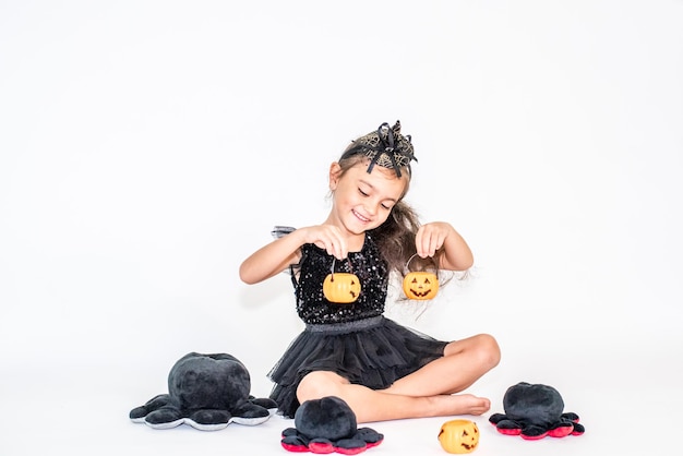 Photo portrait of a little brunette girl in a black hat and black dress in halloween decorations.