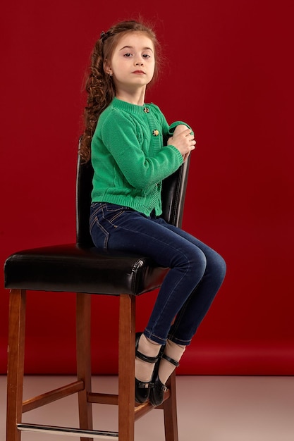 Portrait of a little brunette girl with a long curly hair posing against a red background