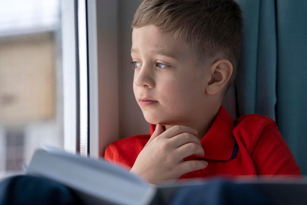 Portrait of a little Caucasian boy who looks out the window sitting at home on the windowsill