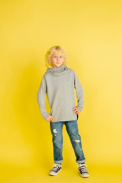 Portrait of little caucasian boy with bright emotions isolated on yellow studio background