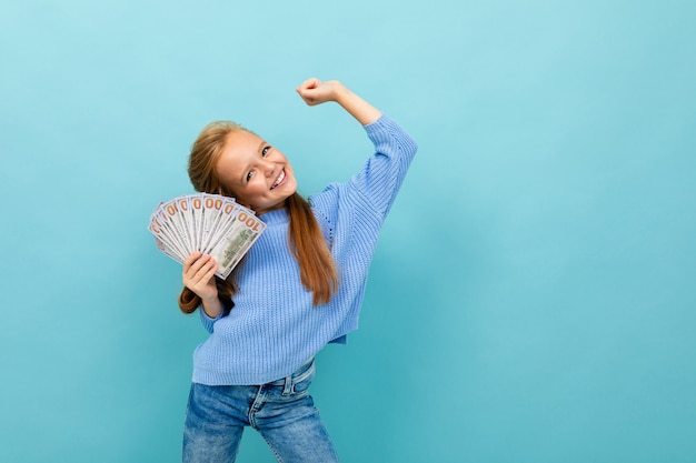 Portrait of little caucasian girl with long brow hair in blue hoody holds a lot of money isolated on blue