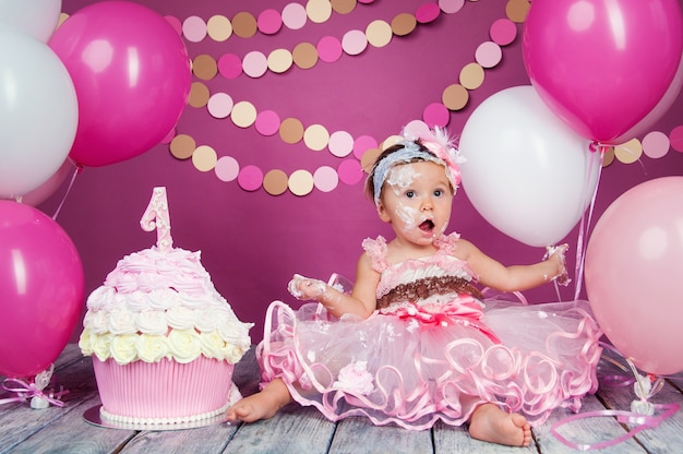 Portrait of a little cheerful birthday girl with the first cake. Eating the first cake. Smash cake.