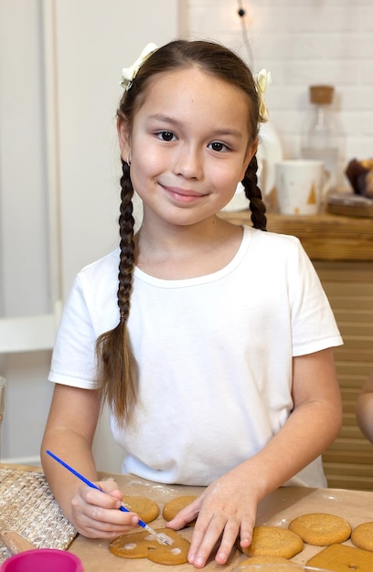 Photo portrait of a little chef at home in the kitchen decorates ginger cookies with icing and powdered sugar for a family holiday