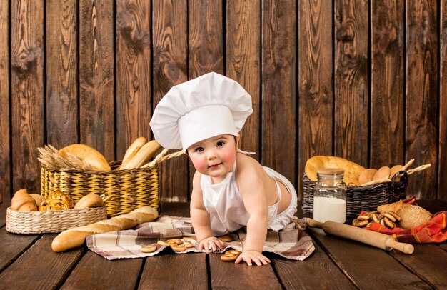 Ritratto di un bambino in abiti da chef tra prodotti da forno su uno sfondo di legno