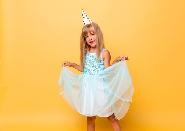 お祝いの帽子と黄色の背景に風船と小さなかわいい女の子の肖像画。