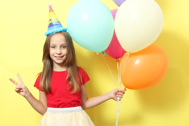 Portrait of a little cute girl in a festive cap and with balloons