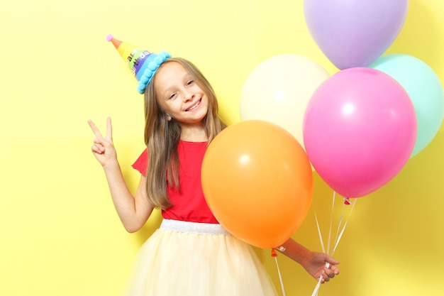 Portrait of a little cute girl in a festive cap and with balloons