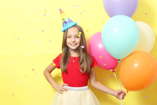 Portrait of a little cute girl in a festive cap and with balloons