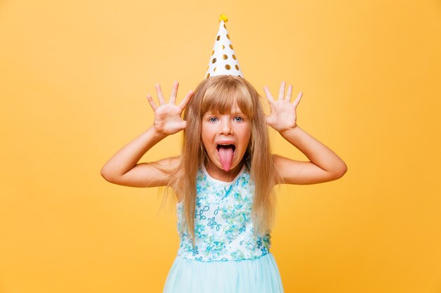 Portrait of a little cute girl in a festive cap on a yellow background. Birthday, holiday.