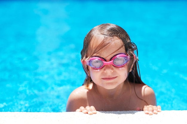 Portrait of little cute girl in the swimming pool Sunny summer day goggles