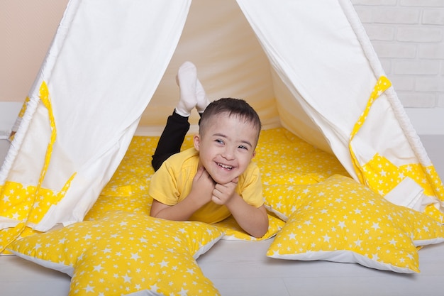 Portrait of a little disabled boy Down who sits in the playroom and smiles.