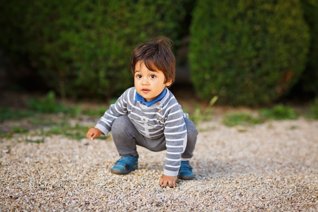 公園で屋外の小石で遊んでいる小さな東部のハンサムな男の子の肖像画。