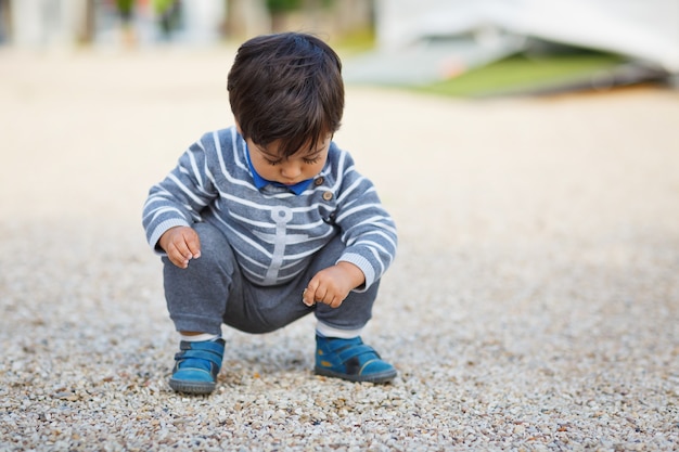 公園で屋外の小石で遊んでいる小さな東部のハンサムな男の子の肖像画。