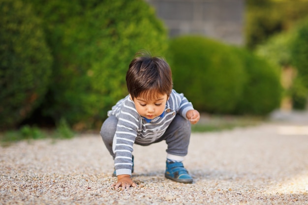 公園で屋外の小石で遊んでいる小さな東部のハンサムな男の子の肖像画。