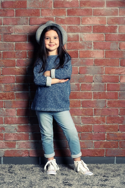 Portrait of little fashion kid girl on bricks wall background