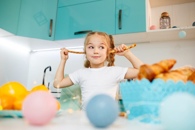 Portrait of a little girl 7 years old sits in the kitchen and plays with bread sticks. Child has breakfast in the kitchen