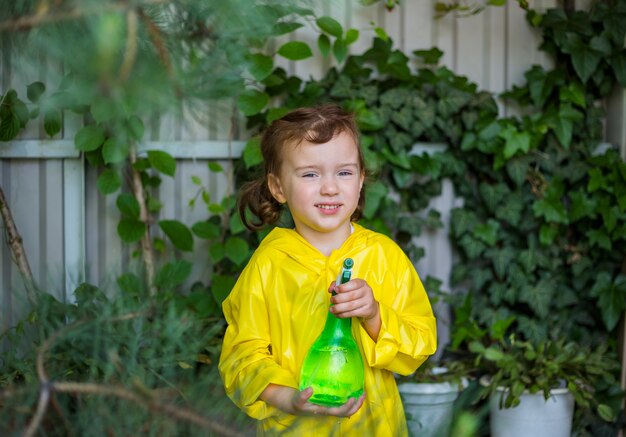 Portrait of a little girl assistant in a yellow raincoat and politization in the greenhouse for plants and conifers