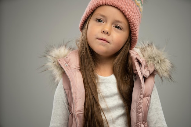 暖かいジャケットと白い背景に分離された帽子でポーズをとって小さな女児の肖像画広告のコピー スペース