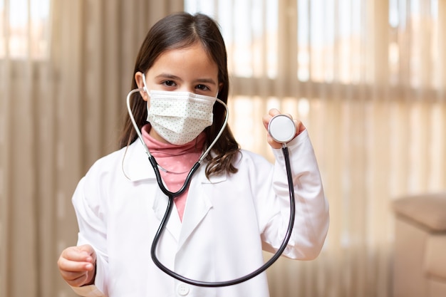 Portrait of little girl dressed as a doctor and medical mask using a stethoscope