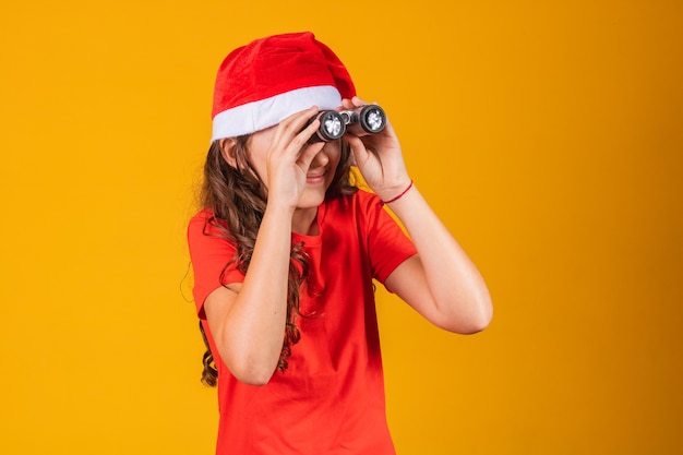 Portrait of a little girl dressed in Christmas outfit looking through a binoculars.