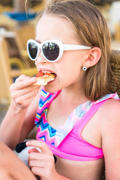 Portrait of little girl eating pizza in outdoor cafe at dinner