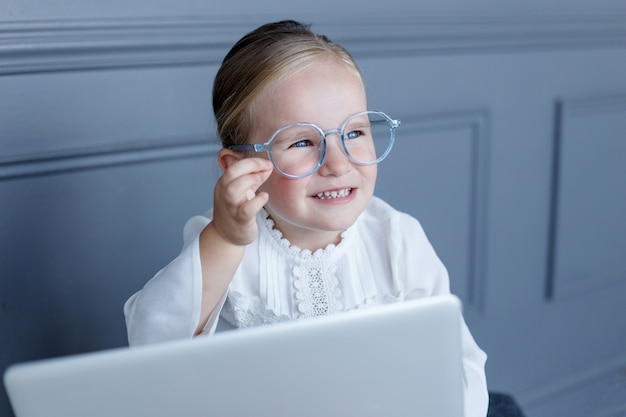 Portrait of little girl in eyeglasses behind laptop