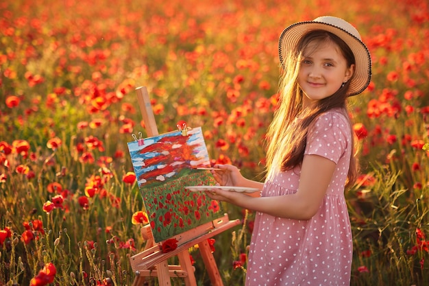 Portrait of Little girl in the field of red poppies On the Sunset and painting on the canvas placed on a drawing stand