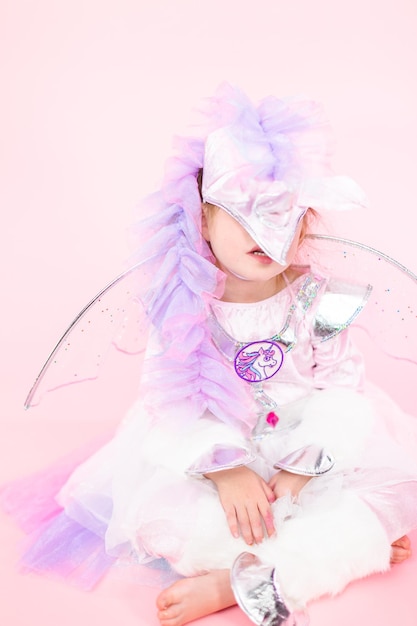 Portrait of a little girl in glitter unicorn costume on pink background.