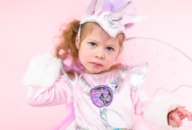 Портрет маленькой девочки в костюме блестящего единорога на розовом фоне.