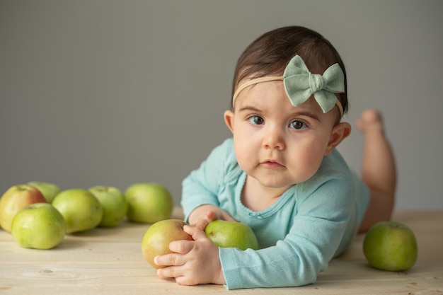 Portrait of a little girl in a green bodysuit on a wooden table with fresh green apples. Natural products for children. High quality photo