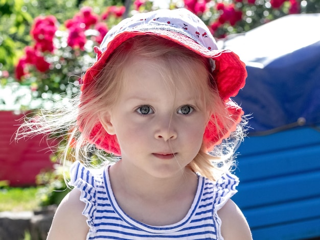 Portrait of a little girl in a hat in a garden near a flower garden