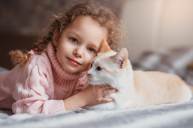 Portrait of a little girl and her pet cat lying on the bed